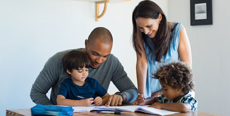 A mother and father at a table with their children doing homework.